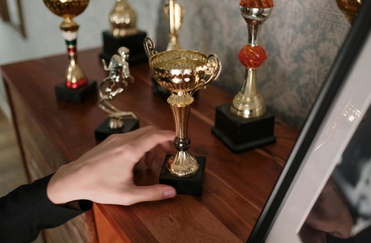 Stella Von Savage Earns Four Cammy Award Nominations A close-up of a hand reaching for a shiny trophy on a wooden shelf, symbolizing success.